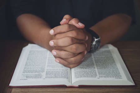 Man with Bible praying, hands clasped together on her Bible on wooden table.の写真素材