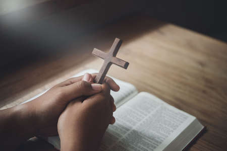 Man holding wooden cross in hands on bible and divine light. Religion concept.の写真素材