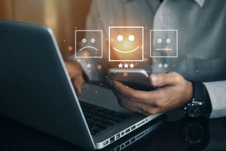 Business man holding phone wiht virtual screen on the happy Smiley face icon to give satisfaction in service. rating very impressed. Customer service and Satisfaction conceptの写真素材