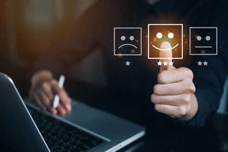 Businesswoman are touching the virtual screen on the happy Smiley face icon to give satisfaction in service wiht laptop computer. Customer service and Satisfaction conceptの写真素材