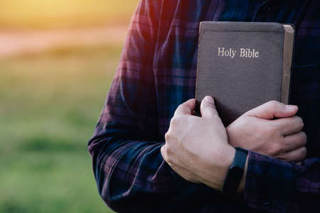 Man in hold and hugging holy bible on the bench. christian praying believe concept.の写真素材