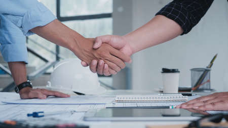Two engineering man with construction worker greeting a foreman at renovating apartment. Engineering objects on workplace with partners interacting on backgroundの写真素材