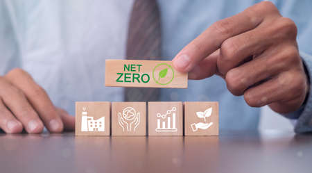 Hand puts wooden cubes with net zero icon in Net zero on grey background. Net zero by 2050. Carbon neutral. Net zero greenhouse gas emissions target. Climate neutral long term strategy.の写真素材