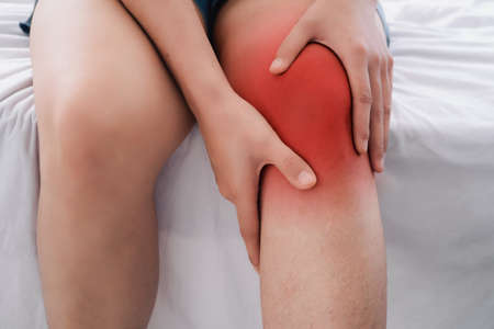 Pain in the knee, man holds hands to his feet, Knee massage, cramp, muscular spasm, red accent on the knee, close-upの写真素材