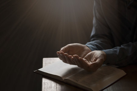 Man praying on holy bible in the morning have a Yellow lights and sparkles coming. Woman hand with...