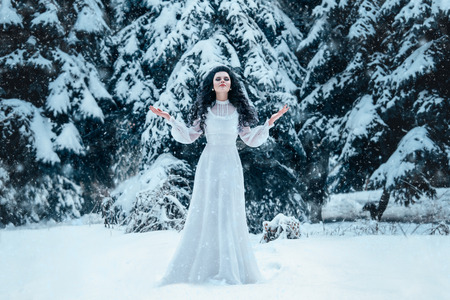Luxury snow queen in a white dress standing on a snowy meadow among the snowy Christmas trees , fashionable toning , Creative Colorsの写真素材
