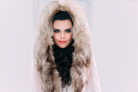 Luxurious brunette in a fur coat with fur hood stands on a snow-covered meadow , fashionable toning , Creative Colorsの写真素材