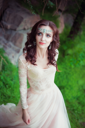 The girl in transparent pastel dress with a train, with a tiara in her hair. Fairy stands on top of the green hills, Creative fashionable color toningの写真素材