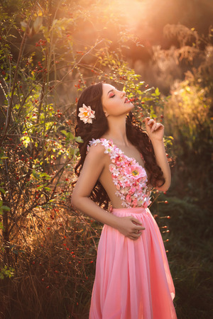The girl in transparent pink dress with a long train flying, decorated with a flower in her hair. Little pink fairy stands on top of the green hills, creative computer color fashionable toningの写真素材
