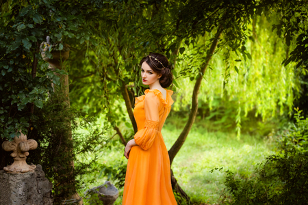 The beautiful countess in a long orange dress  is walking in a green forest full of branches, elf,  Princess in vintage dress, the queen of the forest,fashionable toning creative computer colorsの写真素材
