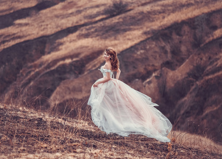 The girl in transparent dress with long flying pastel train stands on the top of the mountain , Shabby chic, boho style , fashion creative computer color renderingの写真素材