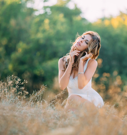 beautiful blonde girl in a light white dress walking in the green fields and spikelets , fashionable toning , creative colorの写真素材