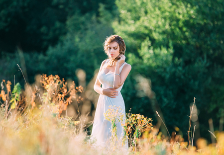 beautiful blonde girl in a light white dress walking in the green fields and spikelets , fashionable toning , creative colorの写真素材