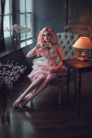 photo session of the girl porcelain doll girl with pink hair sitting on a chair and sees his reflection, baby doll, fashion creative color toningの写真素材