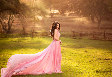 The girl in transparent pink dress with a long train flying,  fairytale princess stands on top of the green hills, creative computer  color  fashionable toningの写真素材