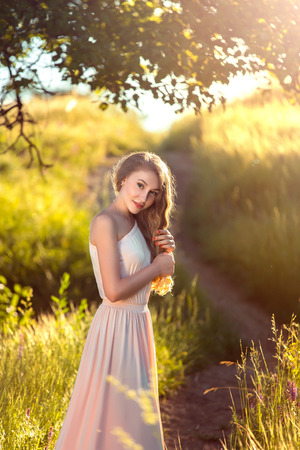 Young luxurious lady in elegant dress pastel tones.Beautiful long hair. Walking along a forest trail. Stylish makeup. Unusual decorations on the background of beautiful nature. Toning fashion. Creative color.の写真素材