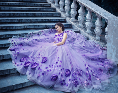 Beautiful, young, brunette in a luxurious, purple, long dress.  Fairy Photo. Creative toning. Queen sitting on the old stairs.の写真素材