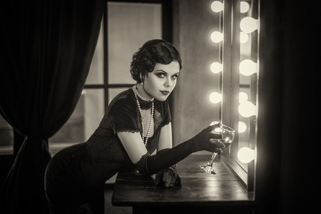 Beautiful Flapper girl with wineglass. Old photo in a retro style. Smokey eyes, hairstyle cold wave.の写真素材