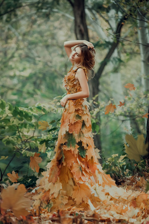 Fantastic girl in the autumn forest. Sad Queen of Nature in a luxurious dress with a leaf. Long hair. Creative colorsの写真素材