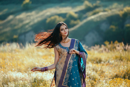 Beautiful girl with dark hair Oriental appearance, dancing among the fields of flowers at sunset. The image on the background of picturesque hills. Fashionable tinted. Creative color.の写真素材