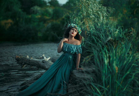 A big beautiful woman. The river witch casts a spell on the water. Green long dress, a wreath of herbs, a fabulous image.Fabulous image. Fashionable toning. Creative color.の写真素材