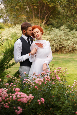 The young bridegroom looks tenderly at his beautiful bride. A girl stands leaning against to him in a beautiful garden. The air is filled with love. The picturesque nature. Fantastic shooting. Retro style. Fashionable toning. Creative color.の写真素材