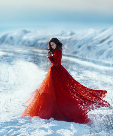 Girl walks in the winter mountains.She dressed beautiful, lush, red dress.Wind waves her clothes.The cold and the snow, creating a fantastic atmosphere photos.Creative colors.の写真素材