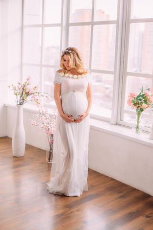 Pretty pregnant woman in white, long dress. Waiting for baby. Fashionable toningの写真素材