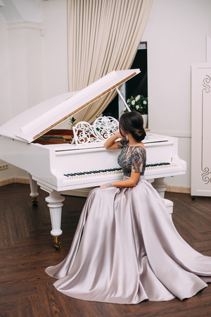 woman in an elegant dress sits near a piano. The luxurious interior.の写真素材