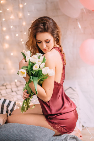 Beautiful brunette girl with long hair, woke up and saw that her room is decorated with balls in honor of her birthday.の写真素材