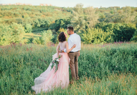 Beautiful wedding in nature. Dress in Boho style. Hairstyle for short hair with flowers. A loving couple is walking at sunset.の写真素材