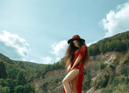 A girl in a red dress is walking posing on camera. In the background is the Carpathians mountains. Creative colors.の写真素材