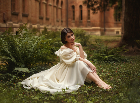 An incredibly beautiful princess sits in the castle garden amid the fern and moss. A beautifully childish face and collected hair is a neat hairdo. On the lady is a vintage ivory dress. Artistic Photoの写真素材
