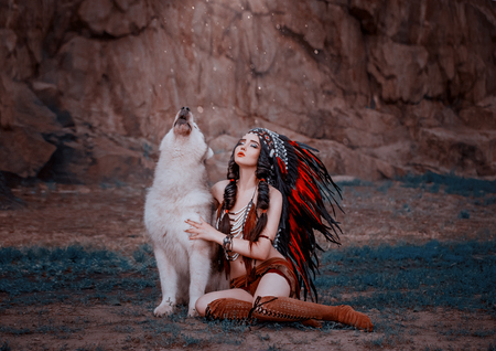 Indigenous American Indian wings with a wolf, a battle cry. The background of the rock. A wild woman celebrates the victory. A luxurious roach with very long feathers. Hairstyle - two braidsの写真素材