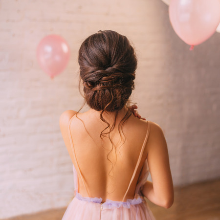 a young attractive lady, a peach dress with a purple color, shows a bare open back and a great neat dark hair hairstyle, standing in a bright spacious room with pink balls, no face in the photo.の写真素材
