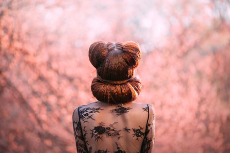 Mysterious lady, with a creative hairstyle pin-up, shooting from the back without a face. Red hair creatively twisted in bagels. Work hairdresser. Background gently pink. Enigmatic woman in lace robeの写真素材