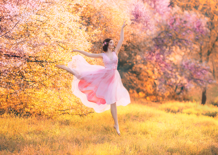 revived porcelain doll in flying pink dress dancing in flowering spring forest, tender lady with dark hair in bright yellow garden, fabulous ballerina enjoys warm days, fairy flight, creative colorsの写真素材
