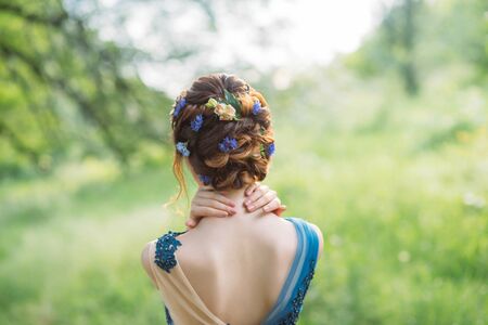 unusual cool chic hairstyle for long dark hair, work of hairdresser, image for graduation and wedding, forest nymph with flowers in a hairstyle, gentle image, an art photo from back without a faceの写真素材