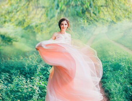 lady and kind Asian beauty in morning spring forest, cheerful joyful girl brightly smiles and flaps lush hem of pink light gentle dress, positive emotions in summer nature, feeling of happinessの写真素材