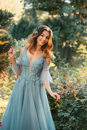 slender lady in light turquoise summer dress with cut on chest and open shoulders, princess with dark hair looks out prince in park, girl with bright smile, positive emotions, art portrait of modelの写真素材