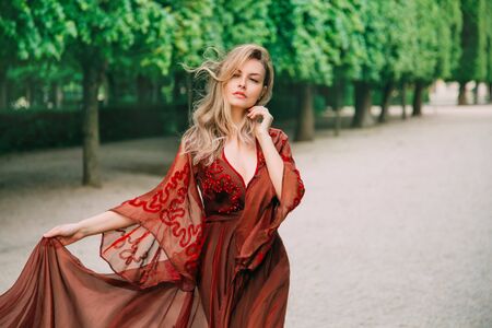 Portrait of a blond woman with flying hair in a red, wine color dress. Gentle makeup, Natural beauty with minimal retouching and without processing. Bloody Countess Bathory. Art horizontal photographyの写真素材