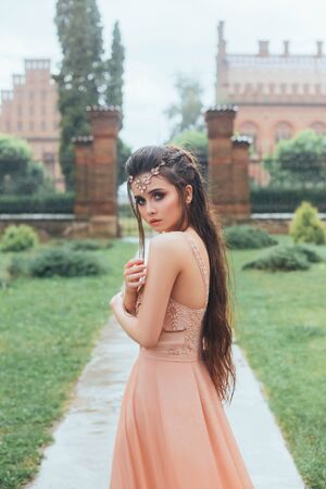 Portrait of a sad, lonely, scared princess who stands frozen and wet in the pouring rain. Incredible, cute face with big eyes, gentle makeup. Tiara on the hair. It stands on the path of the estate.の写真素材