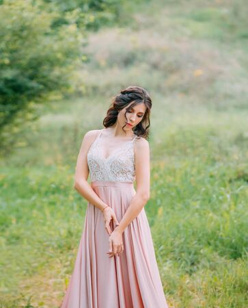 Cute attractive brunette woman enjoying nature in delicate elegant pink silk dress with white lace top. Image for party graduation prom ball stylish evening outfit celebration. Fashion glamor summerの写真素材
