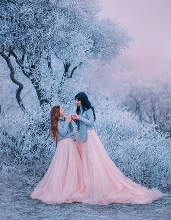 Family photo happy mom daughter look each other love smile face. Cup tea hands. Luxury long puffy gown costume same set warm sweater scarf. Winter fabulous nature tree covered hoarfrost snow ice frostの写真素材