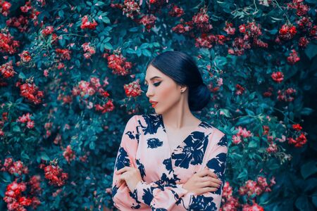 Art Portrait healthy young beautiful woman. Brunette enjoy spring nature fantasy. Pink elegant sexy dress. Backdrop full bloom flowers rose blue trees. Evening holiday makeup red lips, hairstyle bunの写真素材