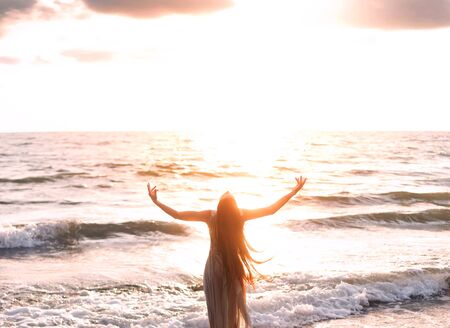 happy woman stands seashore turned away hand raised to heaven sky sun light. Lady girl enjoy sunny...