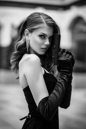 Beautiful dangerous woman spy holding pistol in her hands. retro girl with elegant evening...