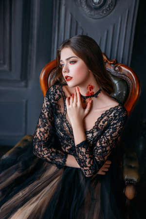 beautiful adult girl, victim of a vampire with a bloody bite on her neck. Young woman in a black gothic dress. Creative makeup and carnival costume for a halloween party. Dark room backgroundの写真素材
