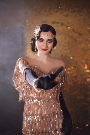 portrait of retro flapper beauty fashion model posing in studio. Happy Woman smiling face. room full smoke. Golden shiny dress, accessories. Girl flirts, shows with hand finger, gesture no, stopの写真素材