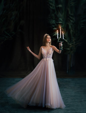 Art photo of medieval girl princess walks runs in dark gothic room. Woman queen is holding candlestick with burning candles in hand. Pink purple dress fly in motion. long blonde hair gold royal crownの写真素材